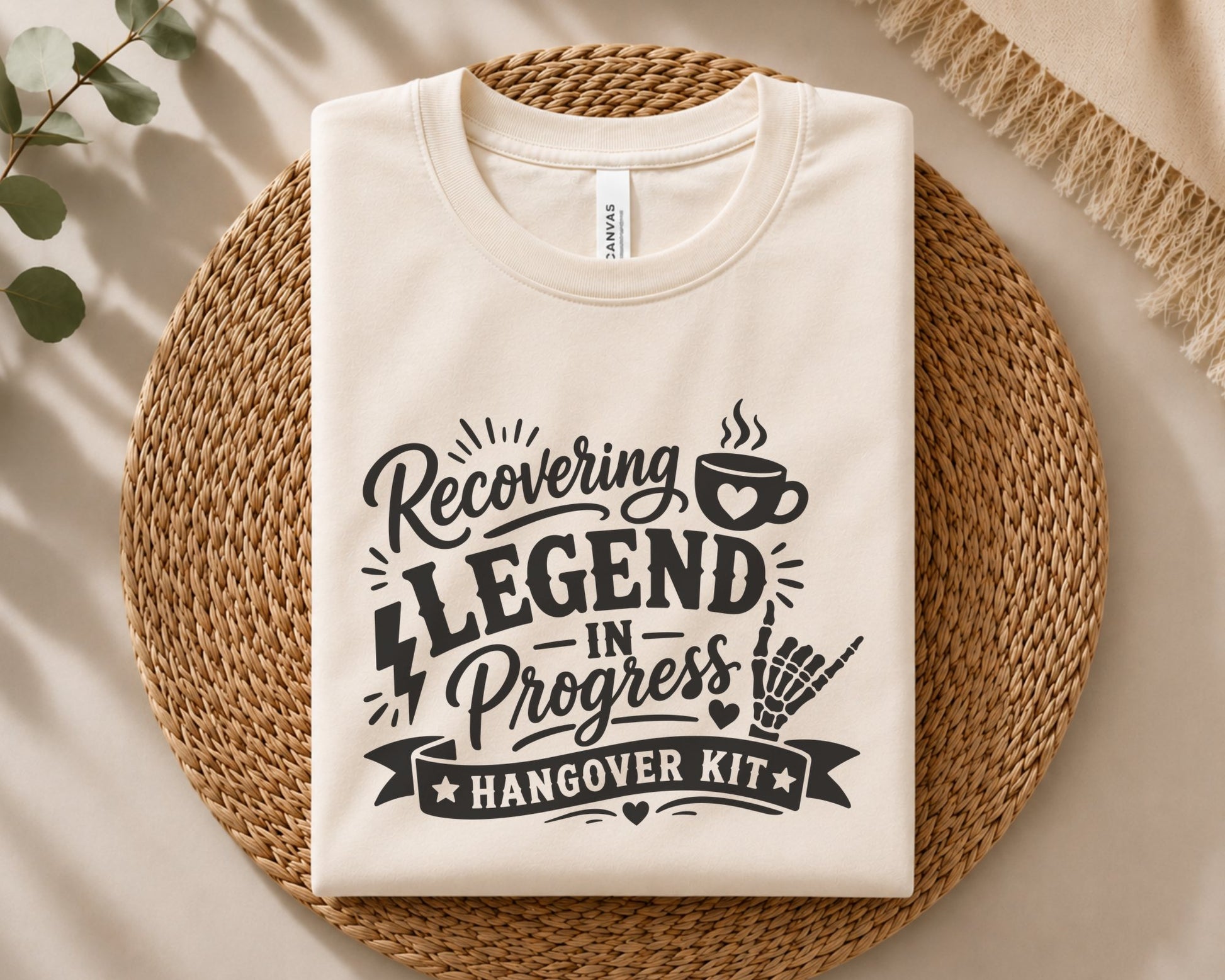 Funny hangover quote design with stacked bold lettering, steaming coffee cup, skeleton hand gesture, ribbon banner and playful decorative accents.