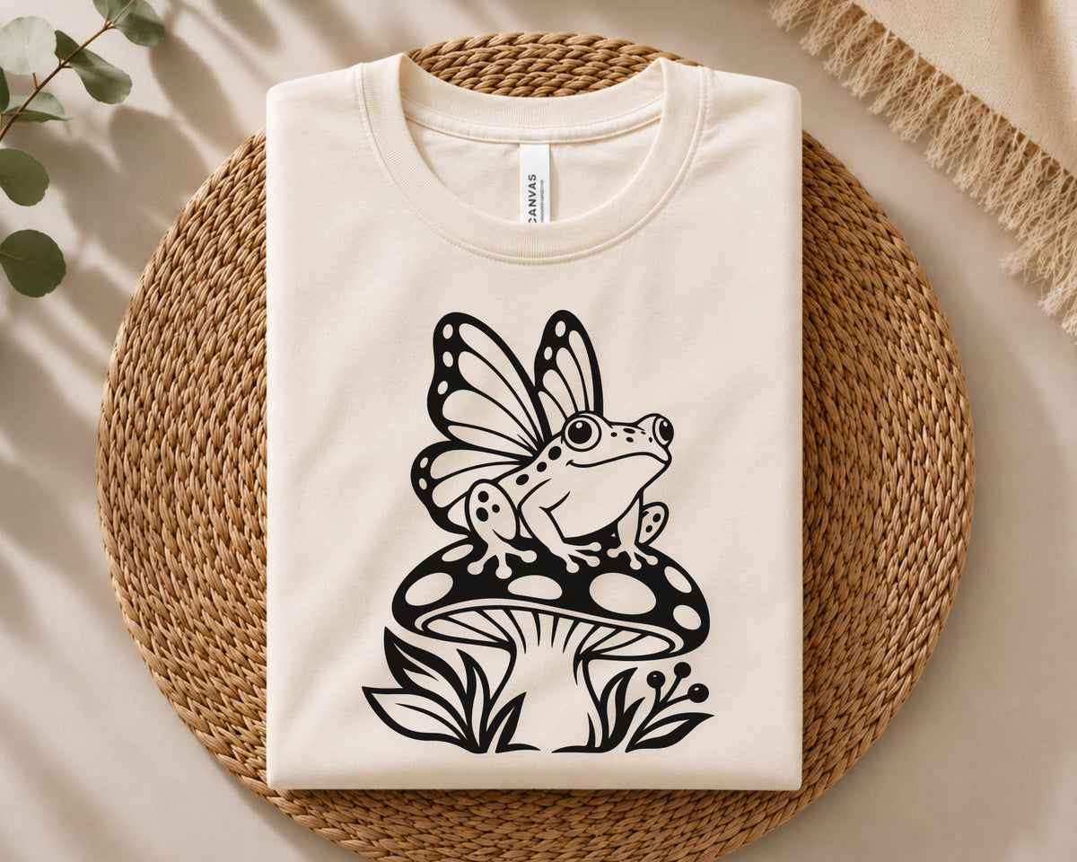 Fantasy frog cut file featuring a winged frog sitting on a mushroom with botanical accents, ideal for shirts, decals, printables, and woodland projects.